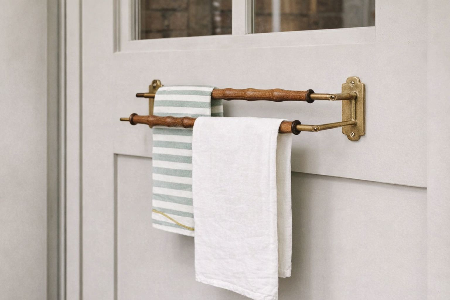 Elegant dubbel handdukshållare i mässing och trä monterad på en ljus dörr.