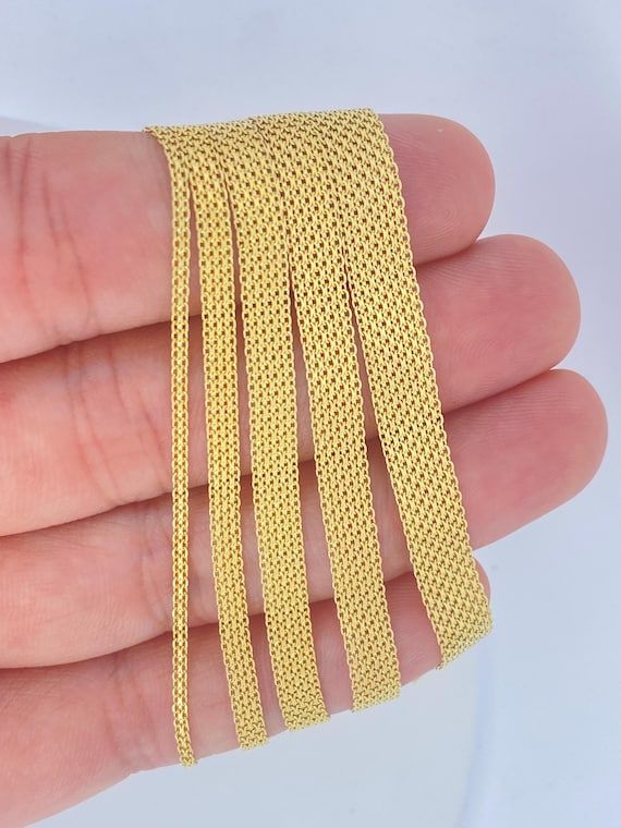 Flera guldfärgade Bismarck-armband i olika bredder som visas över en hand.